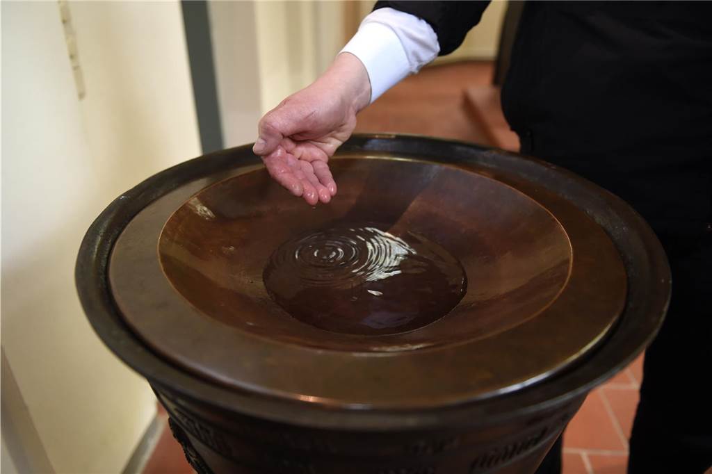 wasser tropft von einer hand in ein taufbecken