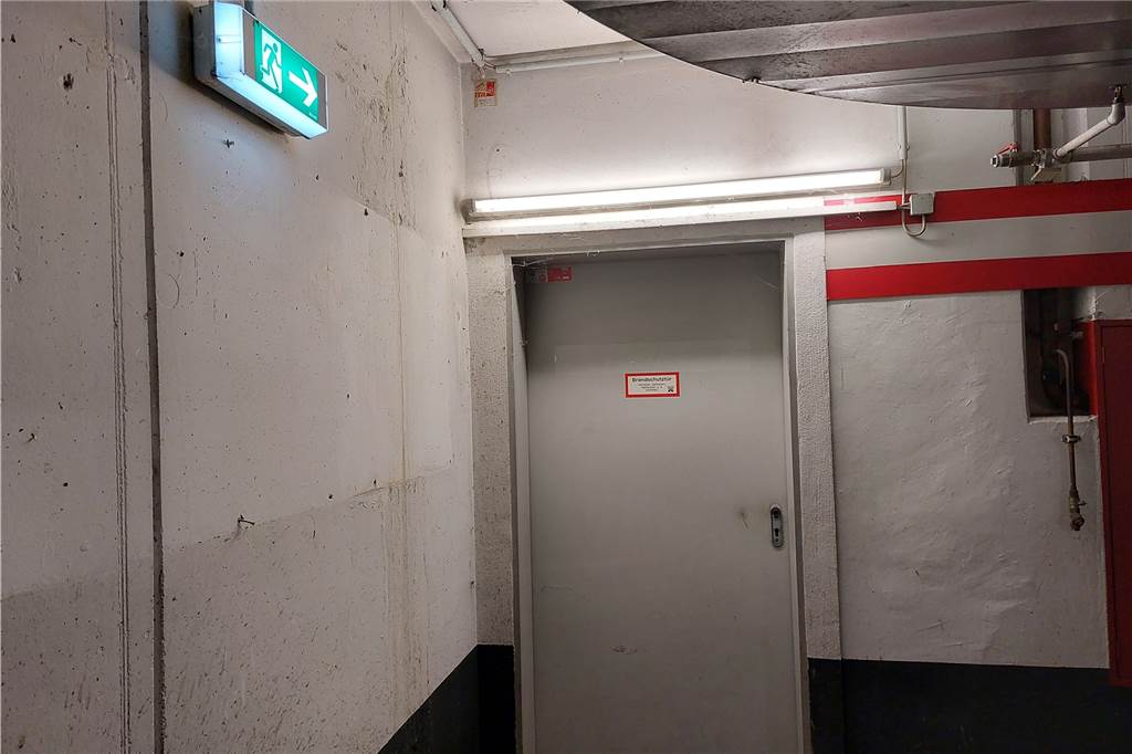 Vandalismus im Toom-Parkhaus: Mehr Videoüberwachung geplant Brandschutztür in einem Parkhaus, worauf ein beleuchtetes Notausgangszeichen zeigt.