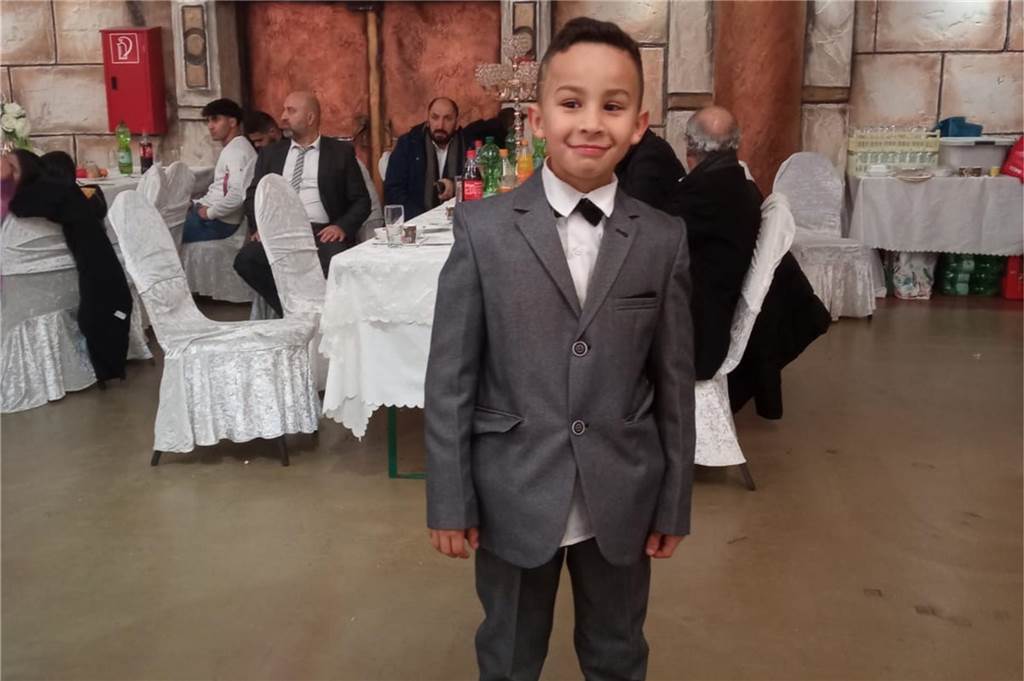 Nach dem Zugunglück: Vater berichtet über Reha-Beginn seines Sohns Amir Ein kleiner Junge steht mit grauem Anzug und weißem Hemd grinsend in einem Festsaal in Recklinghausen.
