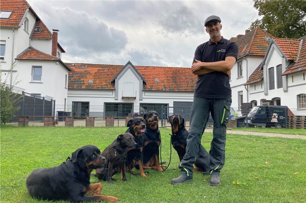 Dirk David Schmitt steht mit verschränkten Armen auf einer Rasenfläche vor seinem Anwesen in Waltrop. Neben ihm liegen seine vier Rottweiler und ein Mischling.  