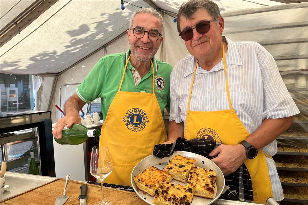 Lünsche Mess bei fast 30 Grad in Lünen: Schausteller: „Das müssen wir leider aushalten“ Dr. Jihad Dabbagh (l.) und Wolfram Zilligen vom Lions Club Lünen verkaufen traditionell Federweißen und Zwiebelkuchen auf der Lünsche Mess.