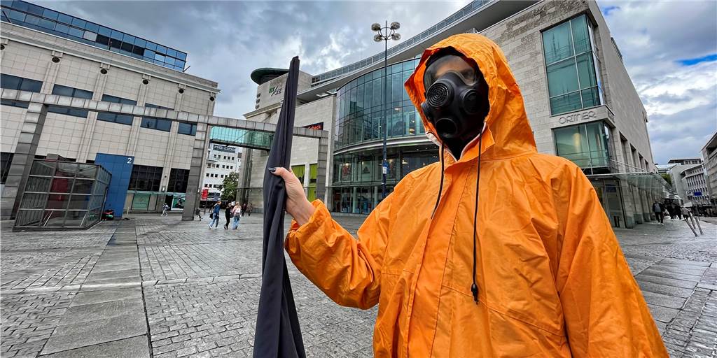Menschen mit Gasmasken und Schutzanzügen schwenken Fahnen in Dortmunds City Drei Menschen in Ganzkörper-Schutzanzügen und Gasmasken waren am Freitagnachmittag mehrere Stunden auf dem Hansaplatz in Dortmund unterwegs.