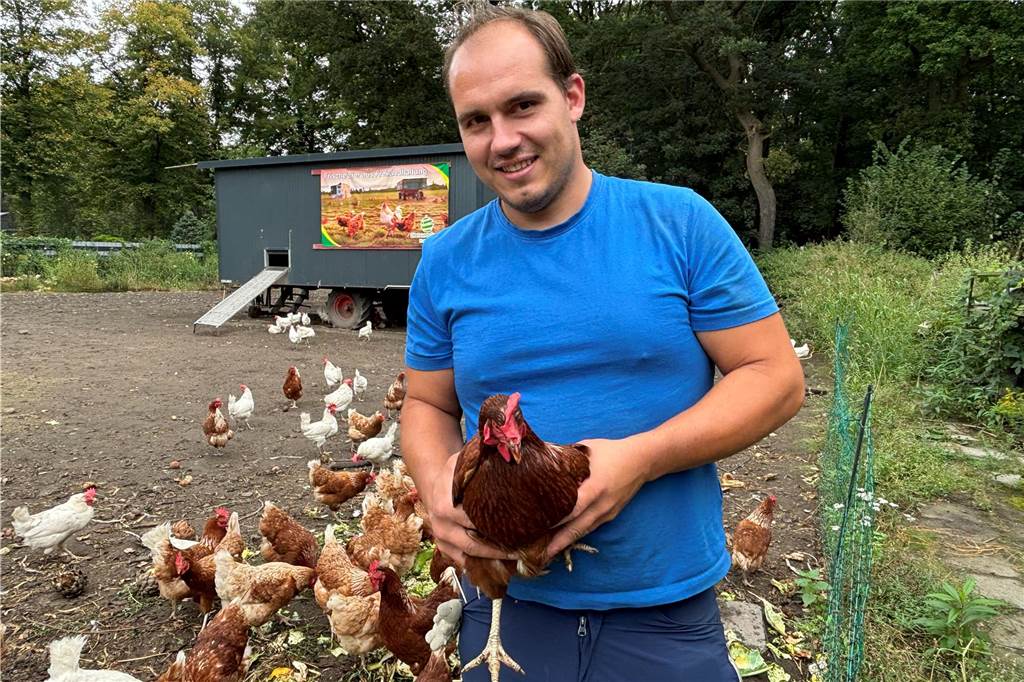 Sascha Michels mit einem Huhn in der Hand. im Hintergrund ein Hühnermobil.