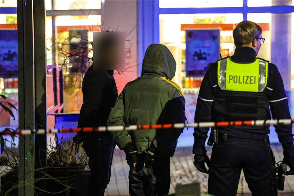 Nach Messerattacke: Erschütterung – und Dank an die Einsatzkräfte Zwei Männer stehen in Handschellen neben einem Polizisten. Sie waren an der Messerstecherei in Schwerte beteiligt.