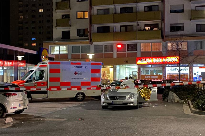 Trauer und Tränen am Tatort in Hanau: „Wir kennen die Opfer alle jahrelang“ Ein Auto ist mit Thermofolie abgedeckt, neben dem Wagen liegen Glassplitter, Rettungskräfte sind im Einsatz.