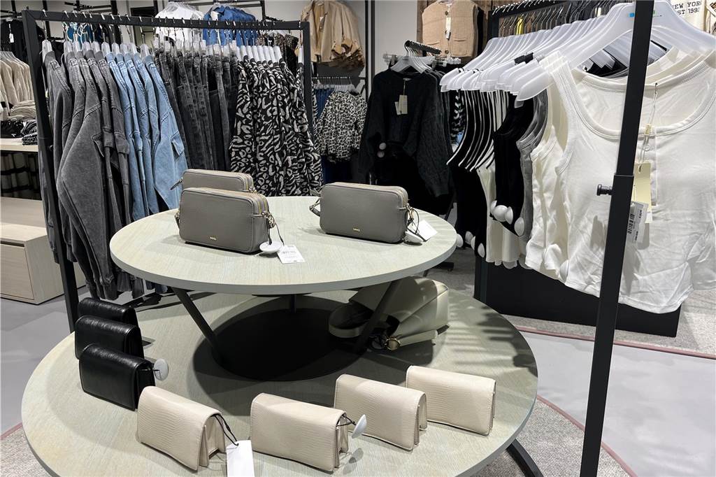 Secilya Yüce zeigt neuen S1-Laden in Mercaden nach dem Umzug Ein Tisch mit Handtaschen steht im S1 in den Mercaden in Dorsten vor zwei Kleiderständern.