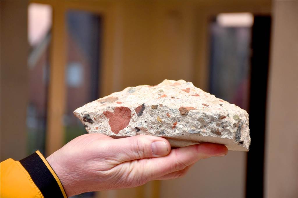 Betonwerk Büscher setzt auf Recycling: Aus Bauschutt entstehen neue Häuser Hans-Jürgen Büscher hält ein Stück einer Betonwand aus Recyclingmaterial in die Kamera. Die Reste von geschreddertem Bauschutt sind an der bunten Körnung des Stücks gut zu erkennen.
