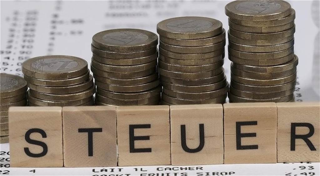 Grundsteuer: Recklinghausen nimmt eine Sonderstellung ein Steuer steht in Scrabble-Buchstaben vor Münztürmen.