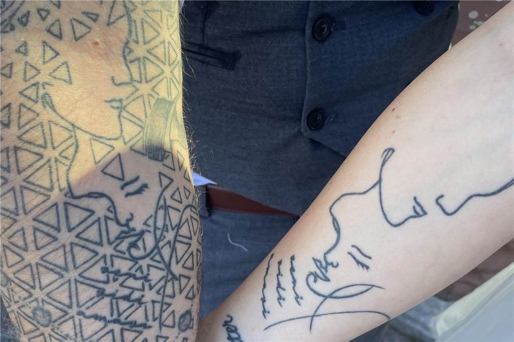 Niclas und Laura zeigen ihr gemeinsames Tattoo auf ihren Unterarmen. Zu erkennen sind ein männlicher und ein weiblicher Kopf. Drei italienische Wörter ergänzen das Tattoo.