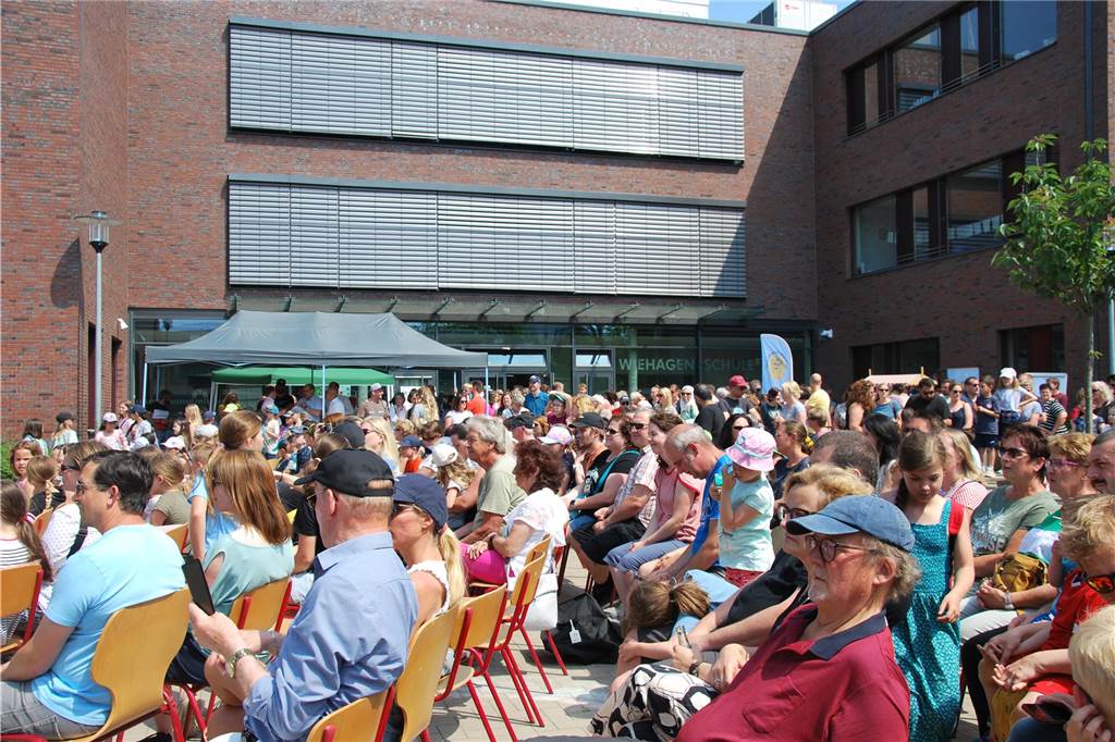 Erstmals im neuen Schulgebäude: Wiehagenschule feiert Schulfest Menschen sitzen auf einem Schulhof.
