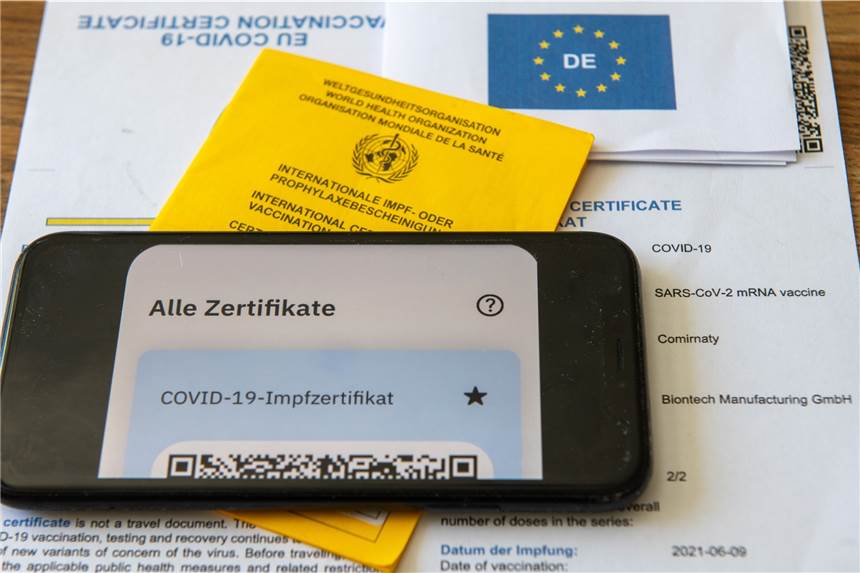 Nach Ausstellungs-Stopp: Impfzertifikate sind in Apotheken schrittweise wieder erhältlich Ein Impfpass und ein Smartphone, auf dem die App CovPass läuft, liegen auf einem Impfzertifikat, das von einer Apotheke ausgestellt wurde.