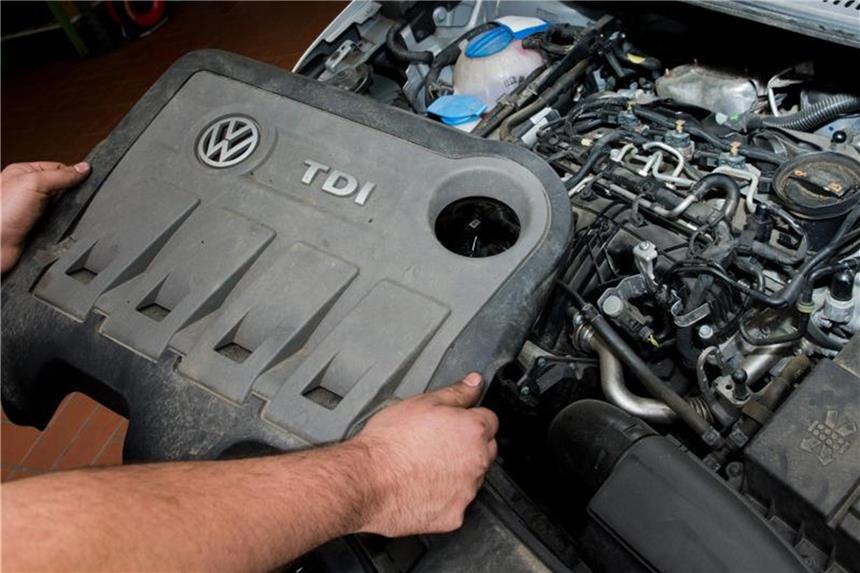Ein Kfz-Servicetechniker in einer Autowerkstatt hält die Abdeckung eines TDI-Dieselmotors vom Typ EA189 von VW. Foto: Julian Stratenschulte