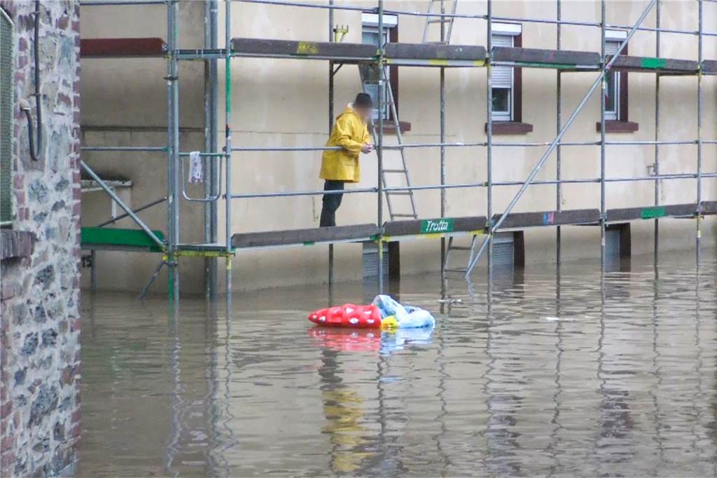 Unwetter in NRW: Zahl der Toten steigt, über Tausend Menschen werden noch vermisst – Liveblog Ein Mann steht auf einem Gerüst und betrachtet die überflutete Straße vor dem Haus in Solingen.
