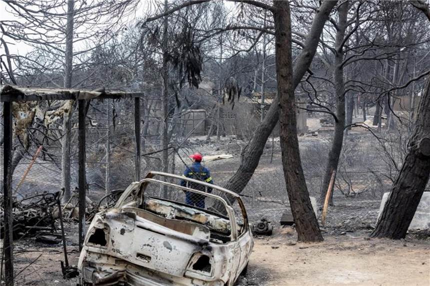 Waldbrände in Griechenland: Was Touristen wissen müssen Ein Mann steht vor einem komplett verbrannten Gelände, nachdem dort ein Feuer gewütet hat. Die außer Kontrolle geratenen Waldbrände haben vielen Menschen das Leben gekostet. Foto: Christoph Soeder