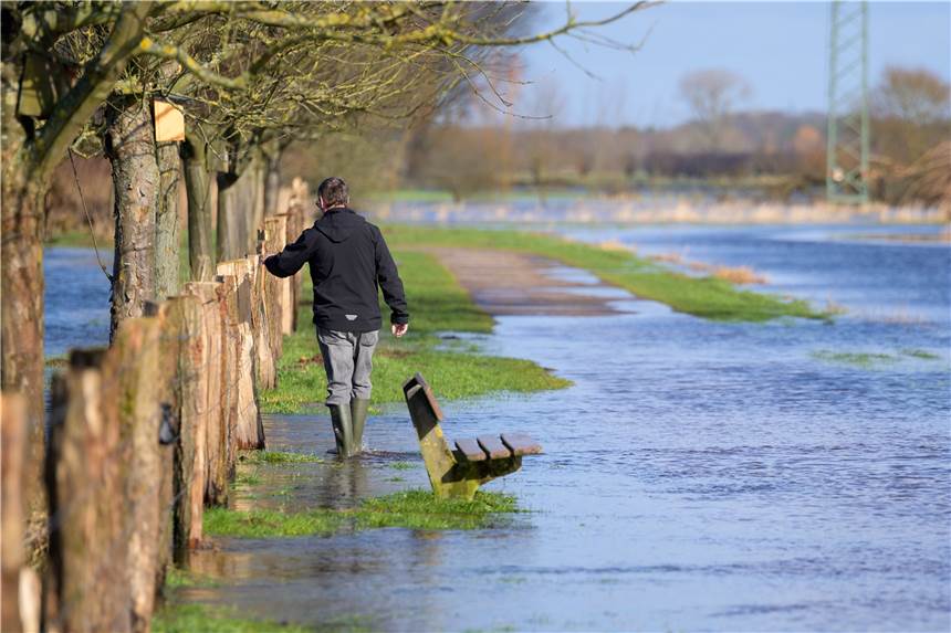 Klimawandel, Hochwasser und Deiche: Steht Norddeutschland bald komplett unter Wasser? Ein Mann watet mit Gummistiefeln durch das Wasser der über die Ufer getretenen Pinnau. Noch sind viele Felder und Wiesen überschwemmt und nicht alle Straßen wieder trocken. Hochwasser-Situationen könnten durch den Klimawandel öfter auftreten.