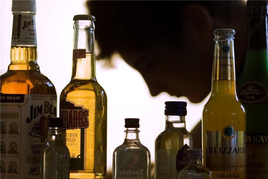 Ein Mensch sitzt hinter Alkoholflaschen. Foto: Jens Büttner/Archiv