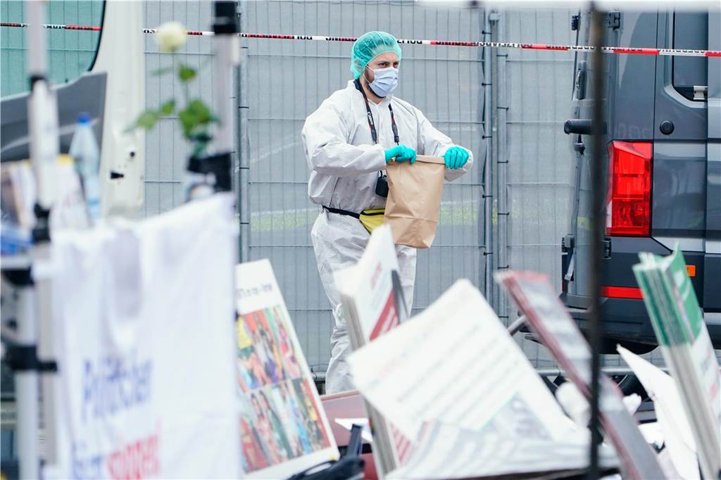 Ein Mitarbeiter der Spurensicherung hält hinter umgeworfenen Plakaten eines Standes eine Tüte in den Händen. 