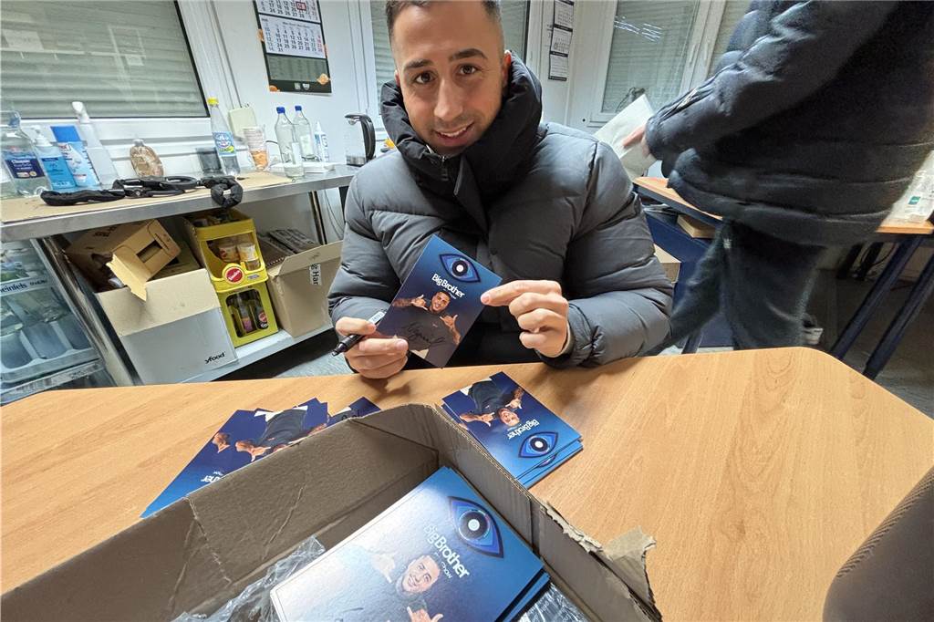 Nadiem Bahjat von Scheidings Lagerverkauf im Big-Brother-Container NAdiem Bahjat an einem Tisch mit seinen Autogrammkarten der Big Brother Show.