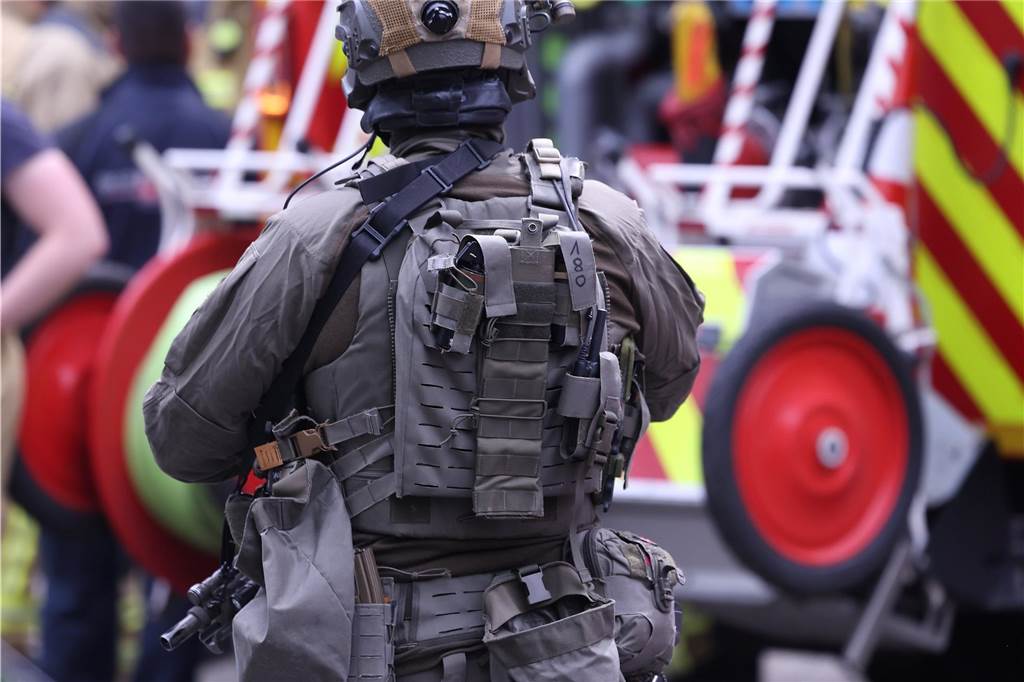 Ein Polizeibeamter steht neben einem fahrzeug der Feuerwehr vor einem Hochhaus. Bei einer Explosion in einem Hochhaus in Ratingen am Donnerstagvormittag wurden mehrere Menschen verletzt - darunter auch Polizisten und Einsatzkräfte der Feuerwehr. Das erfuhr die Deutsche Presse-Agentur aus Polizeikreisen.