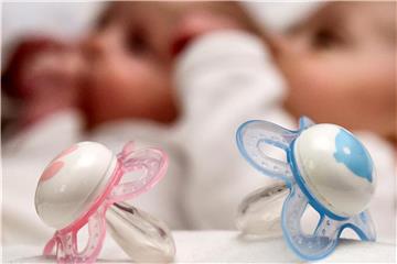 Ein rosa und ein blauer Schnuller liegen vor zwei Babys. Foto: Patrick Pleul/Archiv