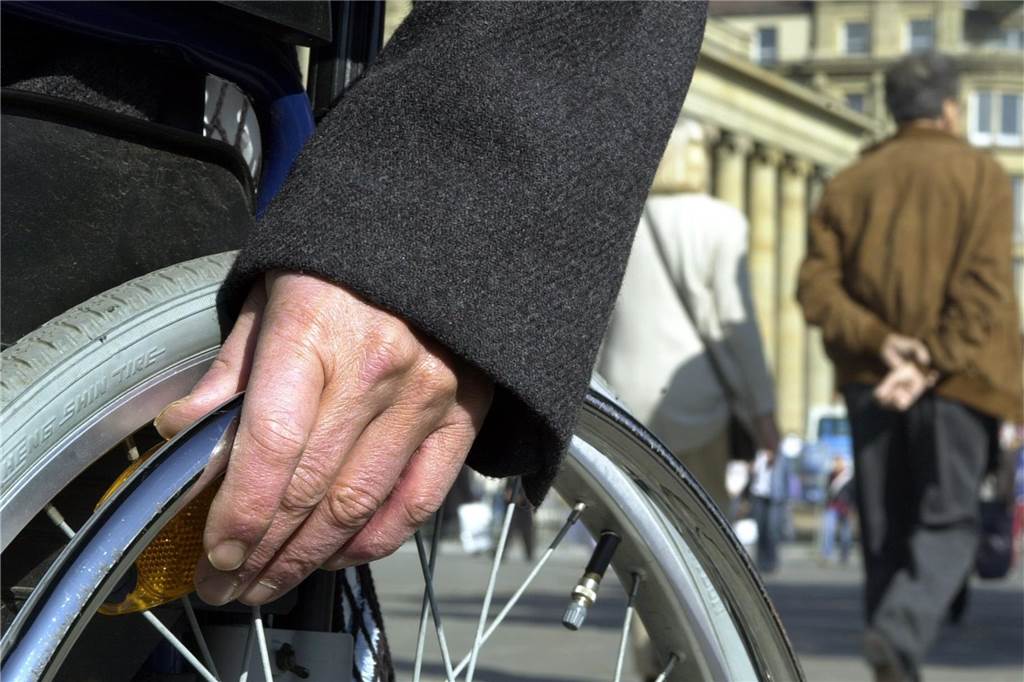 Die Hand eines Rollstuhlfahrers liegt auf dem Rad
