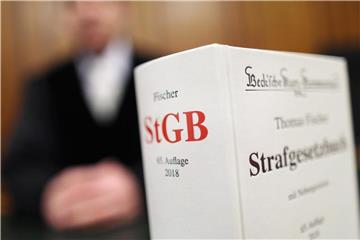 Ein Strafgesetzbuch (StGB) ist im Vordergrund eines sitzenden Mann zu sehen. Foto: Oliver Berg/Archiv