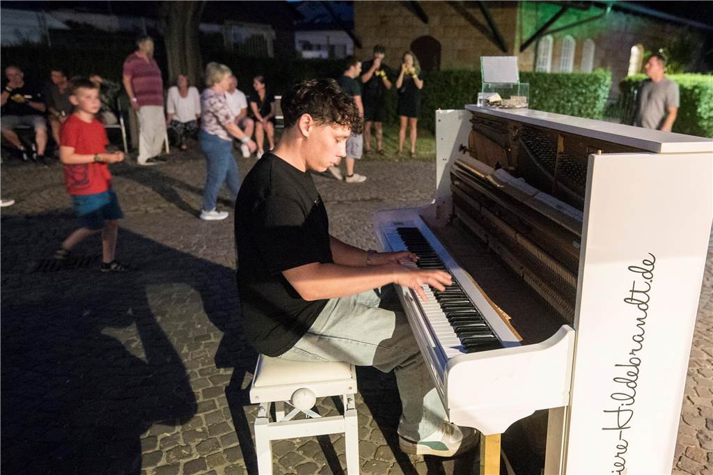Ein junger Pianist spielt in der Dämmerung auf einem Klavier auf dem Gelände des Schiffshebewerks Henrichenburg in Waltrop. Im Hintergrund sind Besucher der Veranstaltung Extraschicht zu sehen.