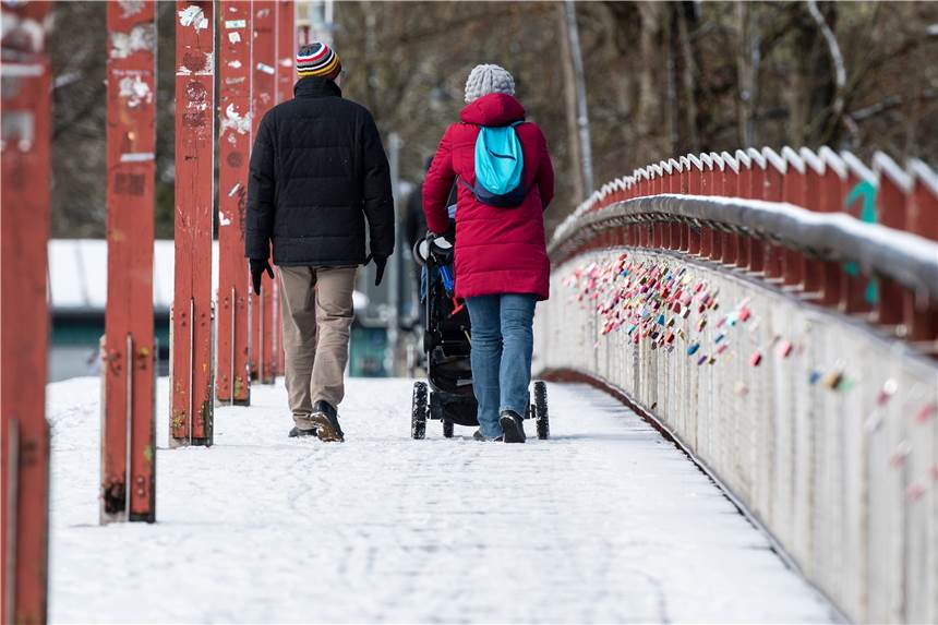 Eine Familie geht mit einem Kinderwagen auf der verschneiten Thalkirchner Brücke spazieren.