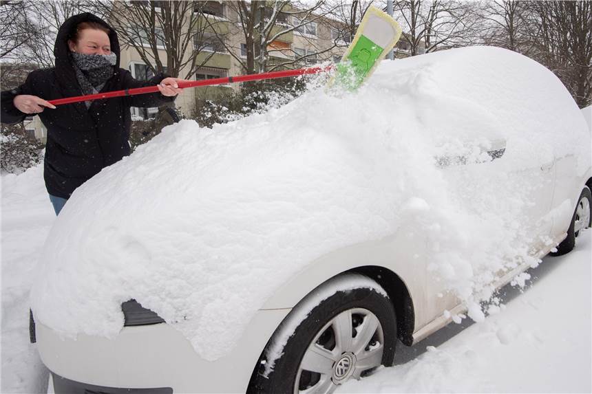 Autofahren im Winter: Das hilft bei eingefrorenen Türen, schwacher Batterie und Co. Eine Frau befreit ihr Auto mit einem Wischer von großen Schneemengen.