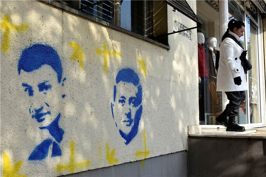 Putin fordert eine neutrale Ukraine: Was bedeutet das? Eine Frau geht aus einem Gebäude, an dessen Fassade in Blau und Weiß, den Farben der ukrainischen Flagge, die Gesichter von Kiews Bürgermeister Klitschko (l.) und Ukraines Präsidenten Selenskyj gesprüht sind.