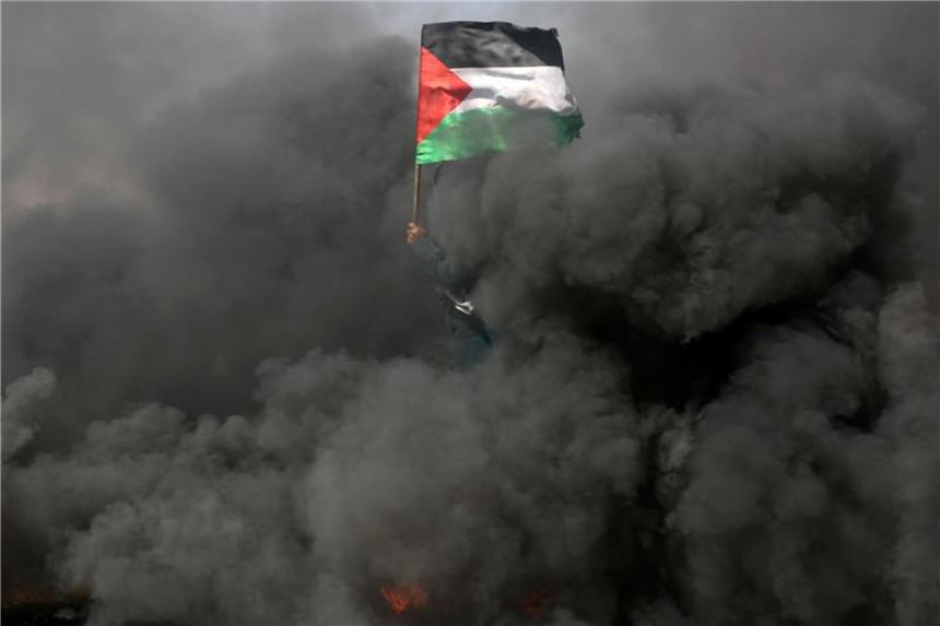 Eine Frau schwenkt bei Protesten an der Grenze zu Israel im Gazastreifen inmitten von Rauchschwaden eine palästinensische Flagge. Foto: Ashraf Amra/APA Images via ZUMA Wire