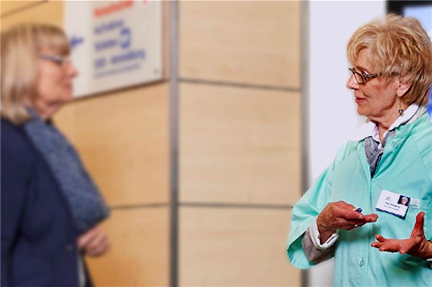 Grüne Damen und Herren kehren zurück in Dortmunder Krankenhaus Eine Grüne Dame bietet einer Patientin am Empfang im Krankenhaus ihre Unterstützung an.