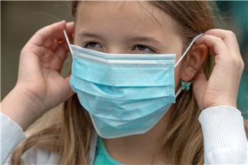 Eine Grundschülerin setzt sich vor dem Betreten eines Schulgeländes eine Einweg-Maske auf (Symbolbild). Eine Unnaerin bezeichnet das Tragen dieser Masken als „Folter“.