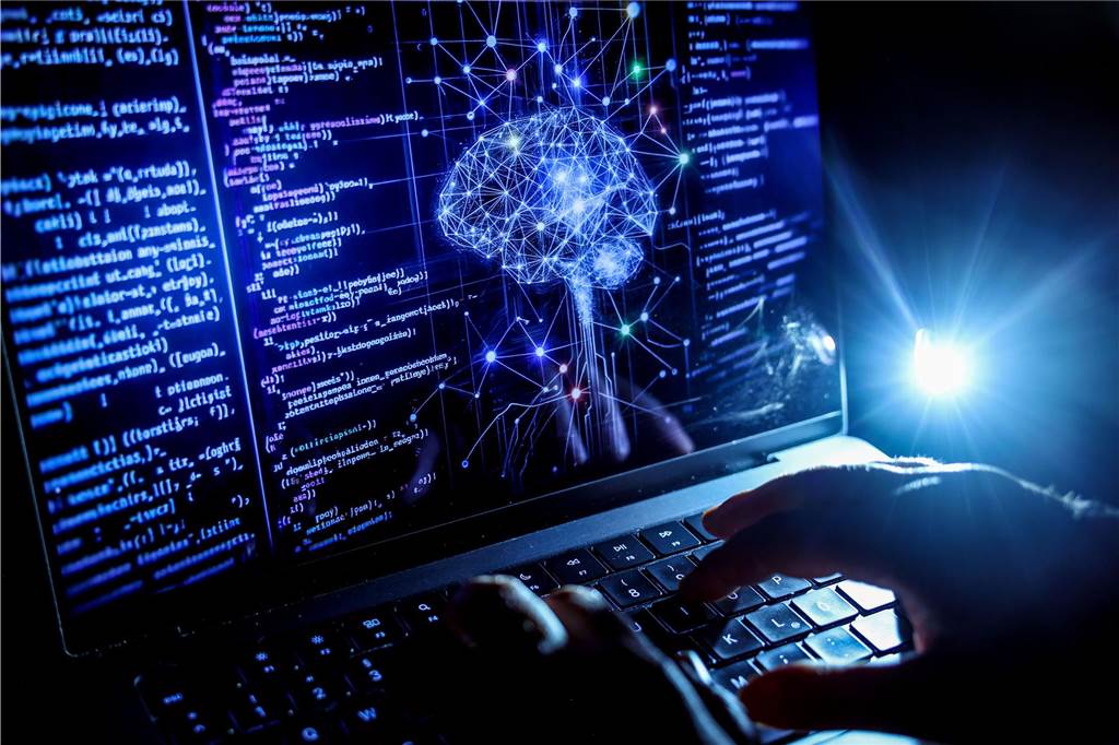 Künstliche Intelligenz verändert die Arbeitswelt: Sorgen und Chancen Eine Person arbeitet hier an einem Rechner, auf dessen Bildschirm ein durch Künstliche Intelligenz generiertes Illustrationsbild mit Code verschiedener Programmiersprachen und einem neuronalen Netzwerk-Diagramm zu sehen ist.