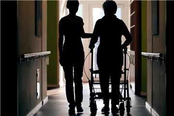 Eine Pflegekraft begleitet die Bewohnerin eines Altenheims mit Rollator beim Gang über den Flur. Foto: Oliver Berg