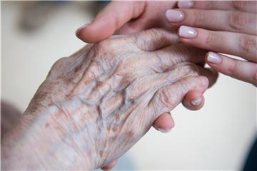 Eine Pflegerin hält die Hand einer Bewohnerin eines Seniorenzentrums. Foto: Christophe Gateau