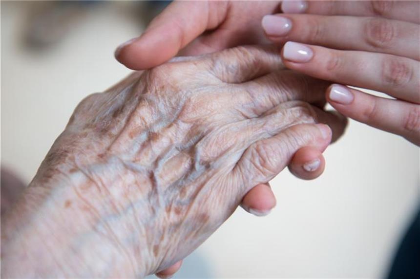 Mehr Geld für Caritas-Mitarbeiter in NRW Eine Pflegerin hält die Hand einer Bewohnerin im Seniorenzentrum. Foto: Christophe Gateau/Archiv