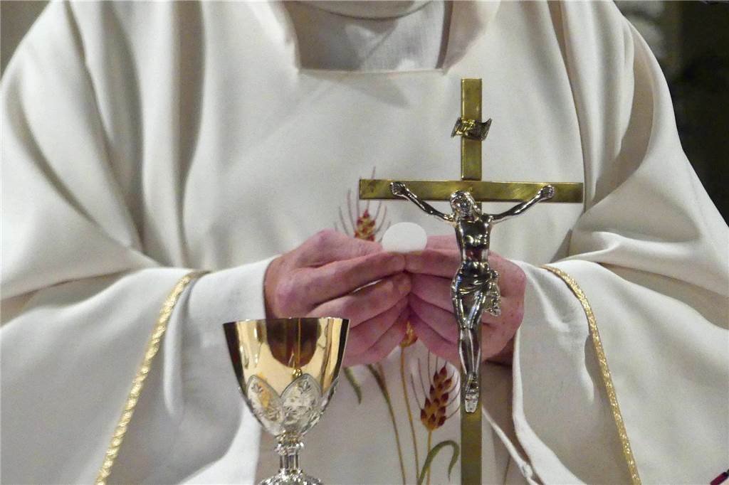 Ein Priester hält ein Kreuz in der Hand.