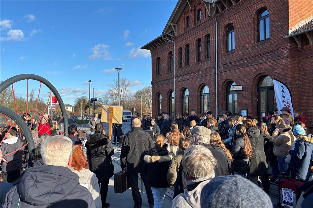 Die Teilnehmer bilden einen Halbkreis um der Rede eine Rede einer Schülerin zu hören. Im Hintergrund ist der Bahnhof zusehen. 