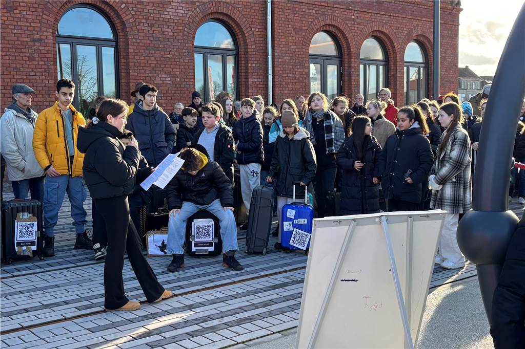 Eine Schülerin hält eine Rede vor dem Bahnhof. Sie liest einen Text vor. Im Hintergrund ist der Bahnhof zusehen. 