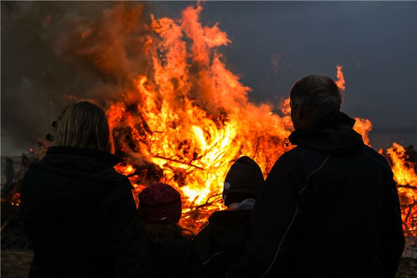 Sicheres Osterfeuer: Mit diesen Tipps vermeiden Sie brenzlige Situationen Eine vierköpfige Familie steht vor den Flammen des traditionellen Osterfeuers und schaut sich das Feuer an.