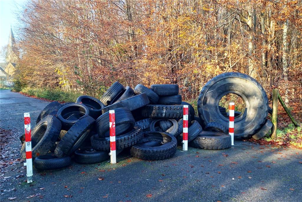Stapel entsorgter Altreifen an Sperrpfosten auf einem Fuß- und Radweg in Dortmund-Mengede. Im Hintergrund: die evangelische Remigiuskirche.