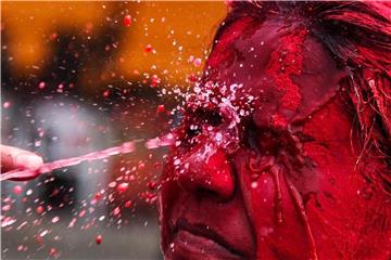 Einer Frau wird Wasser ins rot eingepuderte Gesicht gespritzt. Foto: Stringern.