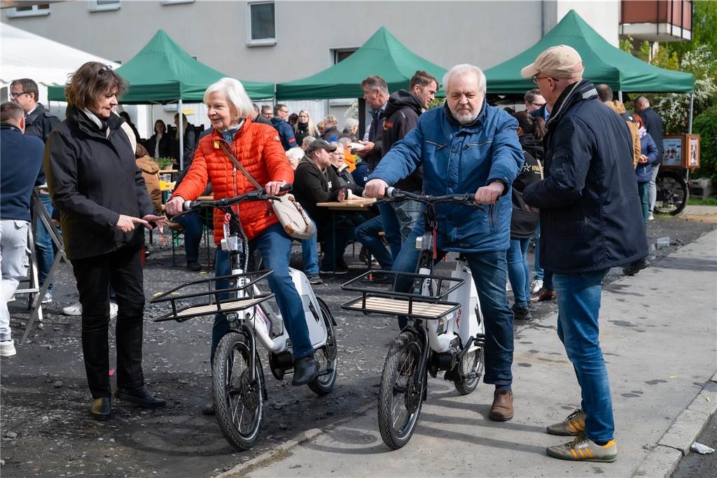 Umzug ums Eck: Monika Franzen lebt seit 55 Jahren im Quartier Mann und Frau testen die Elektro-Lastenräder. Im Hintergrund Pavillons und Besucher beim Mieterfest.