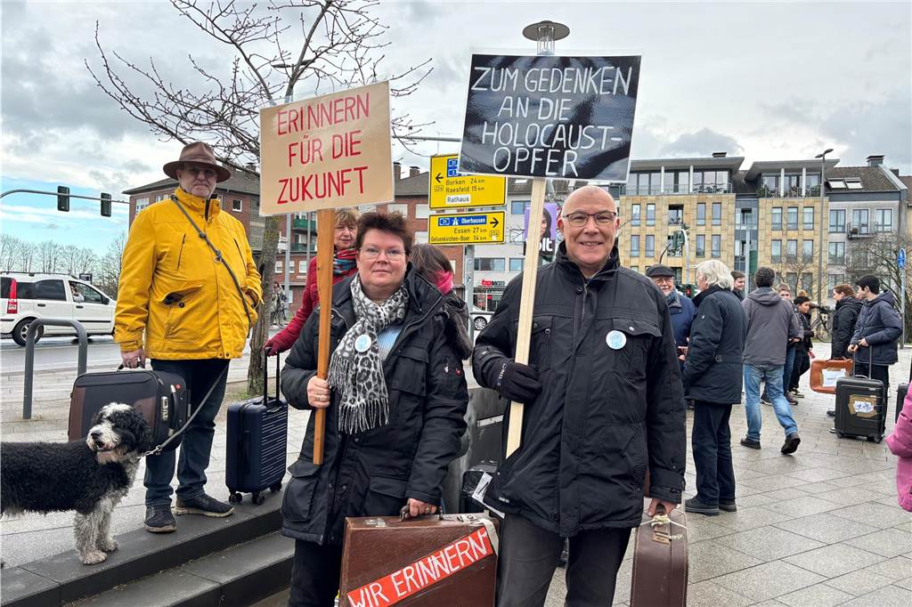 Zwei Personen halten jeweils ein Schild und einen Koffer welche zum Gedenken an den Holocaust aufrufen