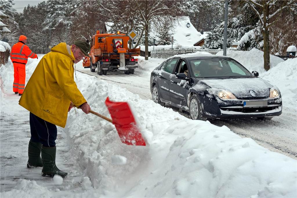 VKU fährt nicht auf Schnee – und ich habe ein Räumfahrzeug verflucht Ein Mann schaufelt Schnee vom Gehweg an den Rand der Straße.