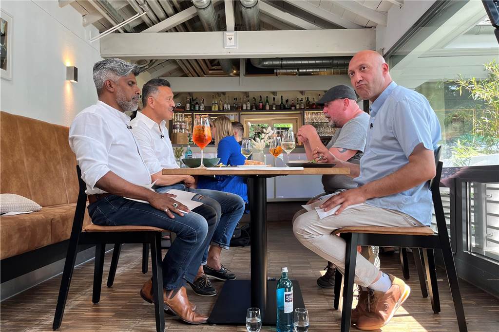 Es gibt Dinge, die stören im Bild: Deshalb haben die Teilnehmer von „Mein Lokal, Dein Lokal“ beim Dreh im Parkbad Süd ihre Wasserflasche, Gläser, Handys und mehr unter dem Tisch liegen. Die vorne sitzenden Gastronomen Mahesh Hewakandamby (l.) und Nunzio Marcucci müssen außerdem ihre äußere Hand auf dem Schoß ruhen lassen, damit auch Nahaufnahmen von den Speisen auf ihren Tellern möglich sind.