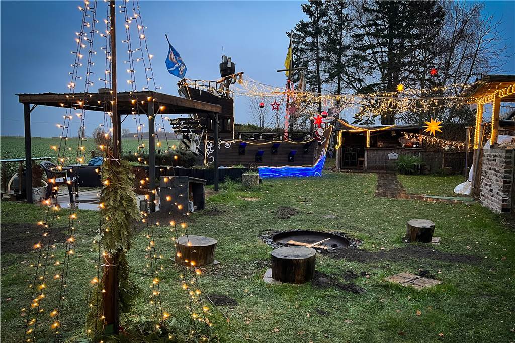 Hans Kett verrät neue Pläne für weihnachtliches Piratenschiff Das Piratendorf von Hans Kett in Dortmund-Lanstrop. Im Vordergrund ein beleuchteter Weihnachtsbaum und im Hintergrund ein Piratenschiff aus Holz mit vielen Lichterketten.
