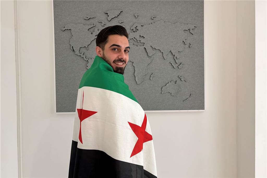 Der Deutsch-Syrer Marwan Abazeid aus Recklinghausen steht mit einer syrischen Rebellenfahne (oben ein grüner Streifen statt eines roten) als Umhang vor einer Weltkarte in der Redaktion der Recklinghäuser Zeitung.