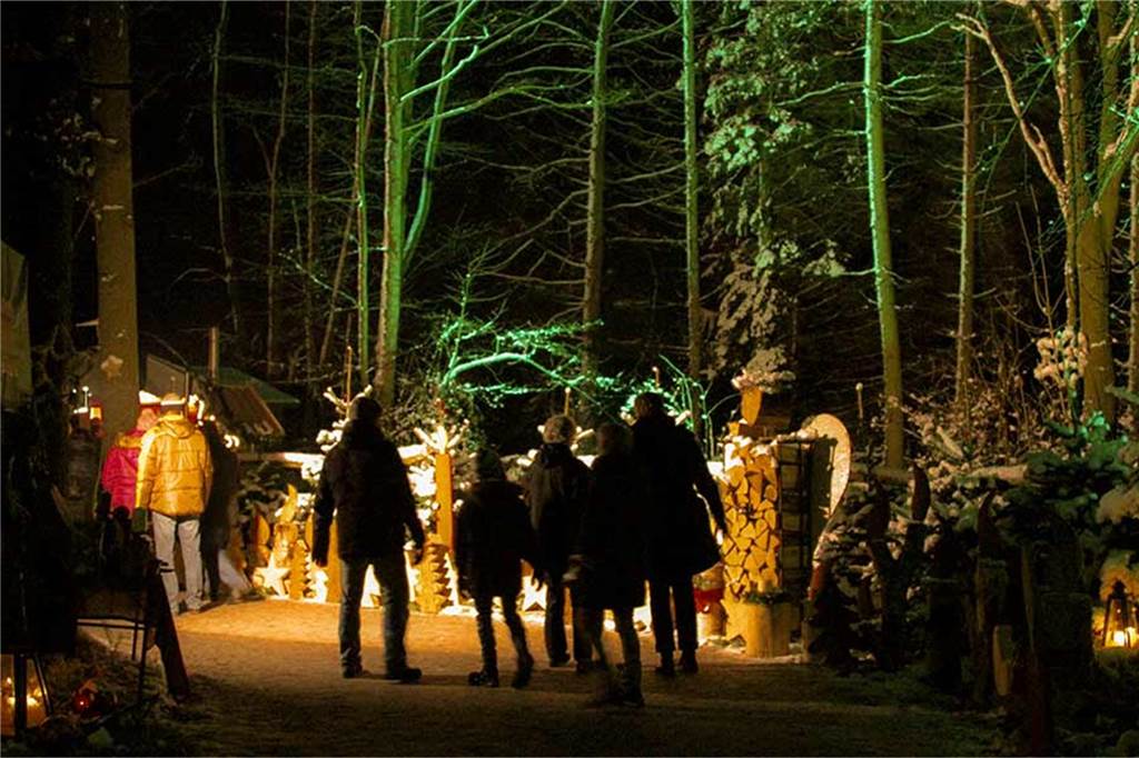 Marbecker Weihnachtsmarkt: Ein ganz besonderer Land–Weihnachtsmarkt Besuchergruppe im Dunkeln von hinten bestaunt einen Handwerksstand auf dem Weihnachtsmarkt.